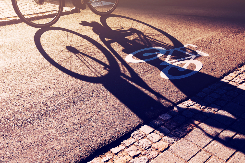 Shadow of unrecognizable cyclist riding a bike on bicycle lane through city street next to the road marking in urban surrounding, retro toned